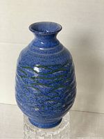Blue ceramic pottery vase with textured blue glaze and green trim detailing visible on the body, shown from the side.