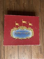 Top view of the red Restoration Hardware Puppet Circus storage box with decorative gold and blue label.