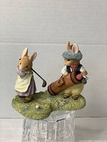 Front view of the hand-painted ceramic Foxwood Tales figurine showing two rabbits playing golf on a grassy base.
