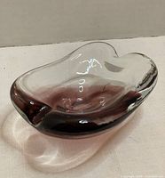 Curved purplish glass art piece with clear glass fused, shown from an angle to highlight shape and color blend.