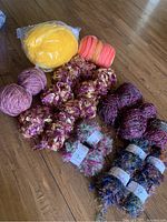 Full view of assorted wool yarns in various colors including yellow, pink, purple and novelty curly multi-color yarns on wooden floor.