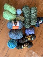 Multiple skeins and balls of wool yarn with green and blue shades on wooden floor