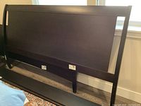 Disassembled king size bed frame leaning against wall showing the headboard and side rails with a very dark brown almost black finish.