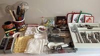 Full view of the assortment on the table showing napkins, napkin rings, flatware in trays, utensils and oven mitts