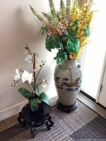 Photo showing full urn with abstract flying crane, tall faux flowers, smaller faux orchid arrangement on wooden stands.
