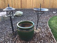 Overview of three items on bark mulch: bird feeder, planter and bird bath