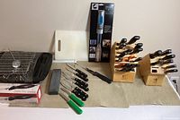 Full overview of all items in the lot including knife blocks, loose knives, carving knives, cutting board, sharpening stone, metal rack, and digital thermometer.