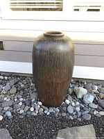 Full view of large ceramic planter vase standing on decorative gravel outdoors near house siding