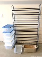 Photo showing the black metal shoe rack on wheels next to stacked five Sterilite storage tubs with lids and two additional small organizers in front.