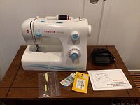 Front view of the white Singer Simple model 2263 sewing machine with power cord, foot pedal, manual, screwdrivers, and needles laid out on table.