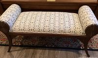 Front view of wooden framed upholstered bench with spiral carved ends and patterned fabric.