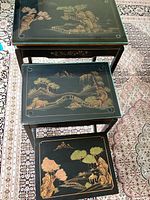 Top view of all three Asian nesting tables stacked, showing different painted landscape scenes on each.