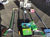 Overview shot of cleaning tools laid out on pavement including brooms, dustpans, mops, and unopened Swiffer pads.