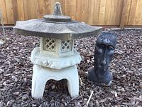Concrete Japanese-style pagoda and dark concrete head planter on ground against wooden fence