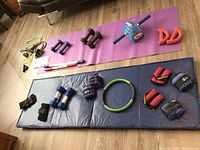 Wide view of full exercise equipment lot showing various weights, hand grips, resistance bands, yoga mats, and ab roller