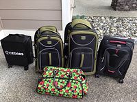 Photo showing all five pieces together: two green and black T-Pro suitcases, one black and red High Sierra suitcase, one small black Cedars hard case suitcase, and one colorful ladybug print duffel bag.