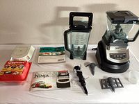 Photo of entire lot showing Ninja blender base, two blender jars, multiple blade accessories, three Ninja manuals, and red Egglettes hard boiled egg maker with lid and rack.