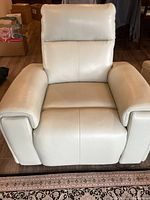 Front view of recliner in upright position showing armrests and cushioned back, off-white leather upholstery
