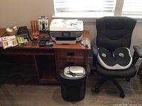 Overview of the desk with the HP printer, paper shredder on floor, office chair with lumbar cushion, and assorted office supplies.