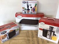 Front view of all four boxed Parini kitchen appliances: immersion blender, electric griddle, 2-slice toaster, and power juicer.