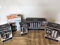 Lot items boxed and arranged including coffee maker, coffee grinder, French press, canister set, and kettle.