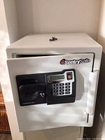 Front view of the white Sentry safe displaying the electronic keypad, fingerprint scanner, and key lock with a set of keys placed on top.