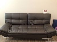 Front view of brown tufted faux leather sofa with chrome legs in upright position