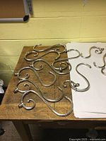 Twelve curved silver plated arms for chandelier on wooden table.