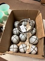 Box containing 12 white stained glass globe lamp shades with metal strips forming a cross pattern, viewed from above showing the globes packed closely together with some brown paper.