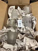 Box of 40 antique glass lampshades wrapped in packing paper, showing variety of frosted and etched designs. Various shapes and styles visible.