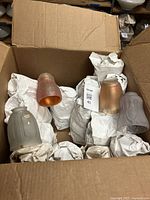 Open box of antique glass lampshades showing five different lampshades and wrapped items inside a cardboard box.