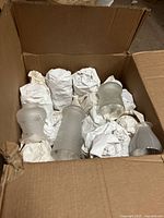 Box containing multiple frosted glass antique lamp shades wrapped with paper to protect them.