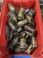 Full view of a red bin filled with various antique brass lamp sockets in used condition, showing mixed types including pull chain and push thru.
