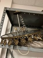 Side view of one chandelier ring showing gold-tone decorative metal frame with leaf motifs and attached crystal bead strands.