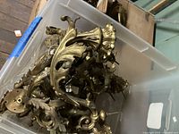View of gilt bronze candelabra and sconce arms piled in a plastic bin showing intricate rococo floral leaf designs and curved shapes
