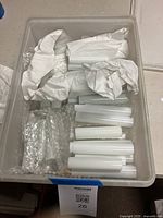 Top view of plastic bin containing many white opaque glass candle covers wrapped in paper and bubble wrap.