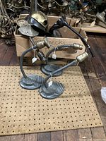 Three antique gooseneck lamps with metal bases and flexible arms placed on pegboard, showing condition and patina.