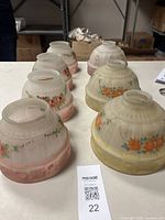 Seven hand painted and reverse painted glass shades shown together, four smaller pink floral and three larger orange floral shades.