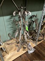 Full view of large Italianate iron chandelier showing base and arms with decorative leaf scroll motifs.