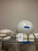 Photo showing large white milk glass globe lampshade with three cream-colored custard glass slip shades on metal shelf.