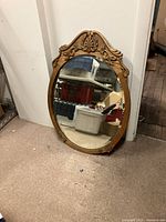 Full view of the oval woods frame and mirror leaning against wall with surrounding storage bins reflected.