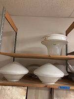 Shelf with three white milk glass schoolhouse lampshades and one Renaissance Revival style ceiling glass fixture with gold decorations