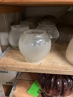 Frosted globe lampshades with etched triangle patterns arranged on a wooden shelf along with dark maroon lampshade visible at the shelf below.