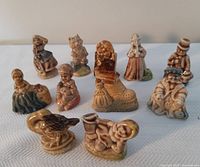 Photo showing 11 Wade Red Rose Tea Nursery figurines in two rows on a white cloth background. Items include children figures, a duck, and other character shapes all glazed in muted browns, creams and blues.