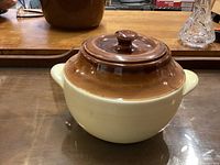 Closed view of the ceramic bean pot showing the brown lid and beige body with side handles.