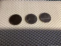 Reverse sides of the three Canadian dollar coins displaying a canoe with voyagers, dates 1968, 1983, and 1986.