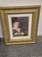 Framed wall art depicting a young child with curly hair blowing bubbles, with a gold decorative frame and ivory matting.