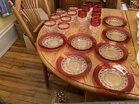 Full view of the 7 ruby rimmed water goblets, 7 champagne glasses, and 7 lunch plates on wooden table