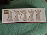 Box art showing all five Mikasa porcelain angel ornaments in different poses with gold hanging tassels.
