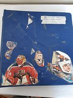 Blue binder with taped label and hockey goalie stickers on cover, showing signs of wear and tear.